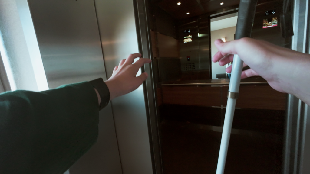 A teenaged girl reaches toward an open elevator door while holding a white cane in their other hand.